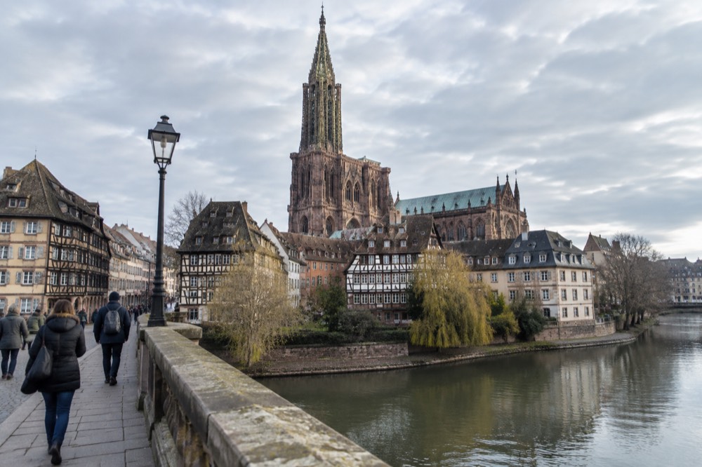 Travellers walking across a stone bridge over the River Ill in central Strasbourg
